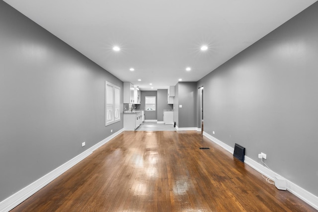 unfurnished living room with recessed lighting, dark wood-style flooring, a sink, visible vents, and baseboards