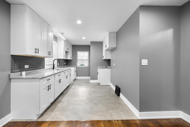 kitchen featuring light stone countertops, white cabinetry, decorative backsplash, and a sink