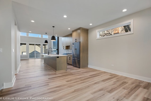 kitchen featuring light countertops, hanging light fixtures, open floor plan, a kitchen island with sink, and high end refrigerator