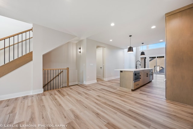 kitchen featuring an island with sink, light wood-type flooring, pendant lighting, and light countertops