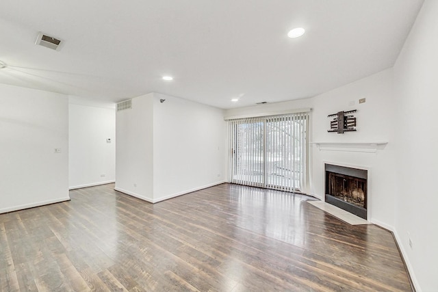 unfurnished living room with wood finished floors, a fireplace with flush hearth, visible vents, and baseboards