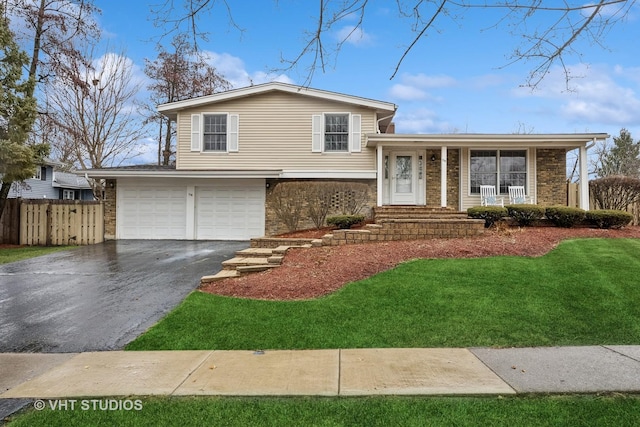 tri-level home with aphalt driveway, a garage, brick siding, fence, and a front lawn