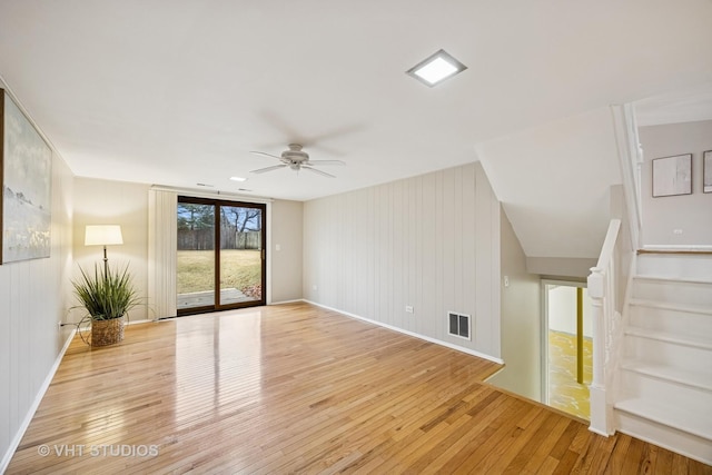 spare room with visible vents, baseboards, light wood-style flooring, ceiling fan, and stairs