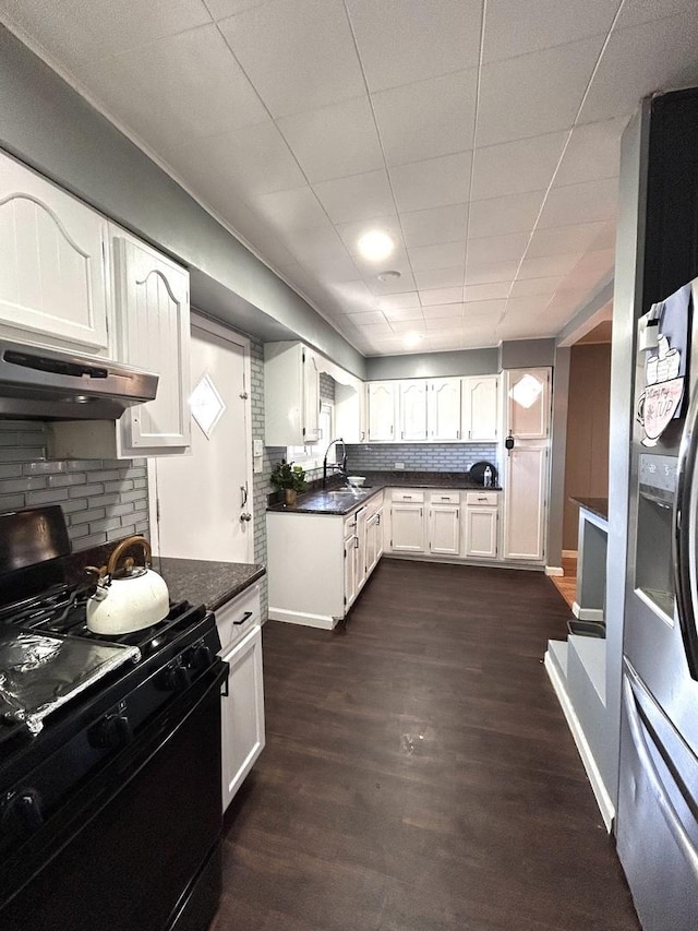 kitchen with black gas range oven, stainless steel fridge with ice dispenser, white cabinets, under cabinet range hood, and dark countertops