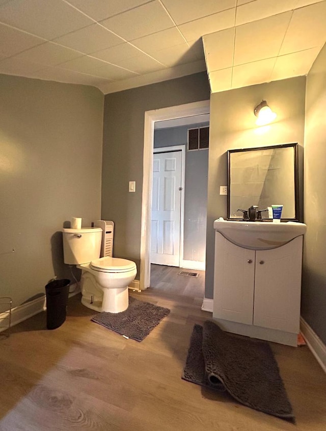 half bath with vanity, wood finished floors, visible vents, baseboards, and toilet