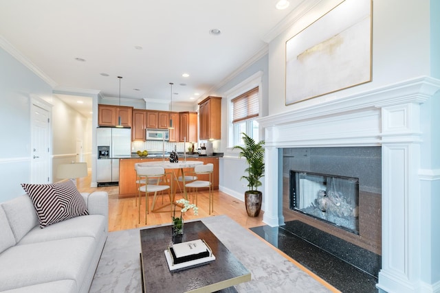 living area featuring baseboards, a tiled fireplace, ornamental molding, recessed lighting, and light wood-style floors