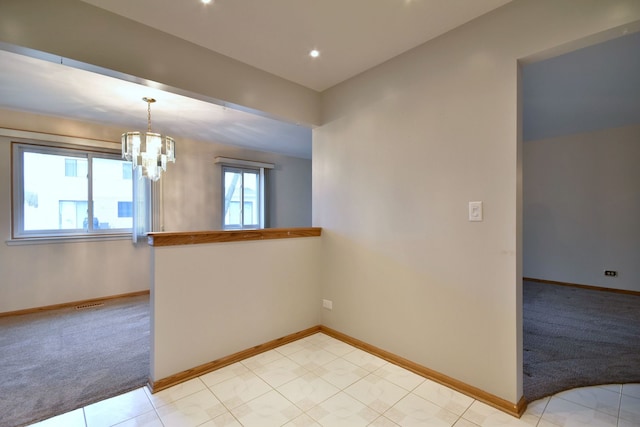 spare room featuring a chandelier, light colored carpet, visible vents, and baseboards