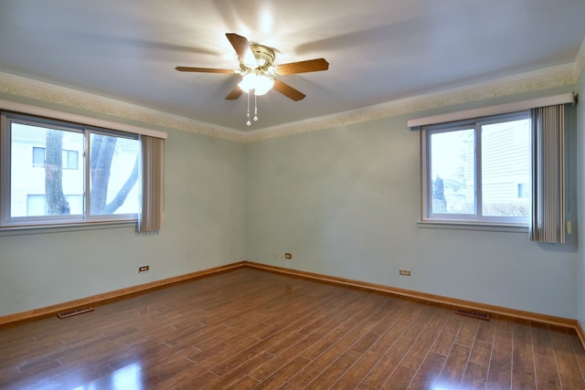 empty room with baseboards, visible vents, wood finished floors, and ornamental molding