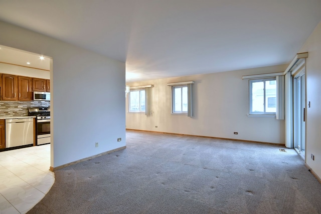 unfurnished living room featuring baseboards, light colored carpet, and a healthy amount of sunlight