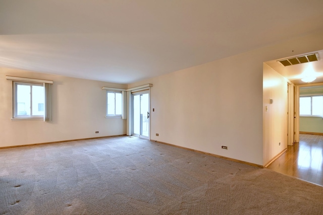 spare room featuring a wealth of natural light, visible vents, and light colored carpet