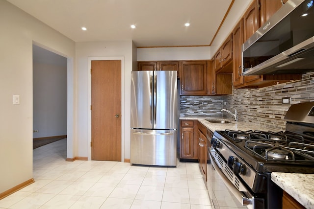 kitchen with stainless steel appliances, backsplash, a sink, light stone countertops, and baseboards