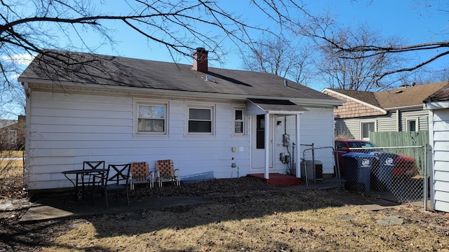 back of house featuring a shingled roof, fence, and a chimney