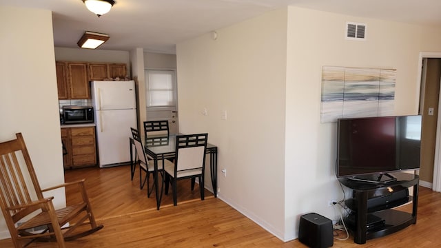 kitchen with visible vents, brown cabinets, freestanding refrigerator, light wood-style floors, and black microwave