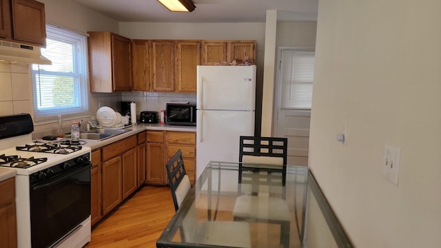 kitchen with gas stove, freestanding refrigerator, a sink, black microwave, and under cabinet range hood