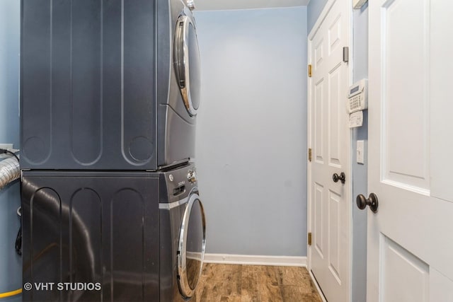 washroom with baseboards, stacked washer and clothes dryer, wood finished floors, and laundry area