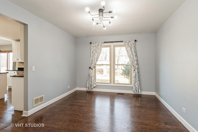 empty room featuring dark wood-style floors, visible vents, a chandelier, and baseboards