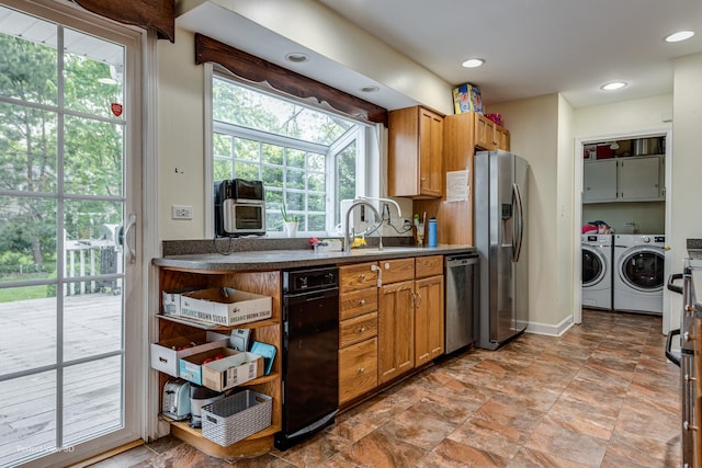 kitchen with washing machine and clothes dryer, stainless steel appliances, dark countertops, brown cabinetry, and a sink