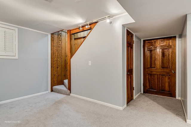 finished below grade area with stairs, baseboards, track lighting, and light colored carpet