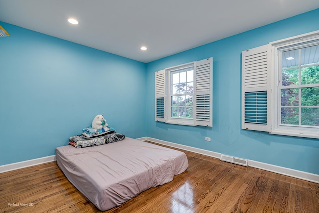 bedroom with wood finished floors, visible vents, baseboards, and multiple windows