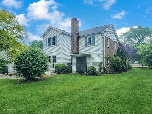 back of house with brick siding, a lawn, and a chimney