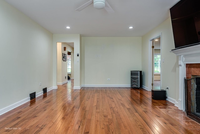 unfurnished living room with ceiling fan, light wood-type flooring, a tiled fireplace, and baseboards