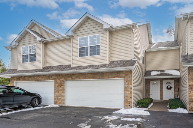 view of property with driveway, roof with shingles, and an attached garage