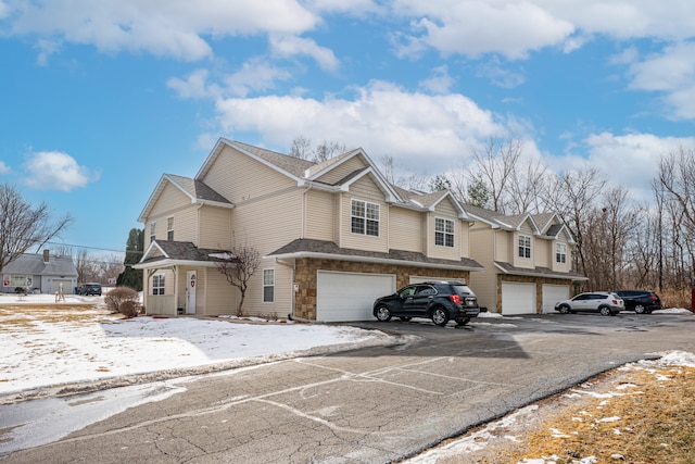 view of front facade featuring a garage, stone siding, driveway, and a residential view