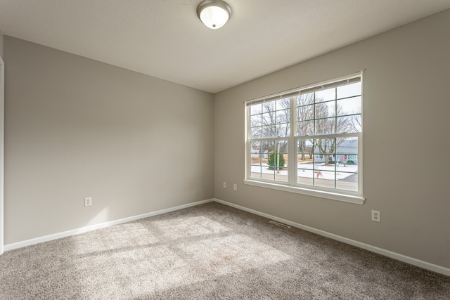 unfurnished room with carpet, visible vents, and baseboards