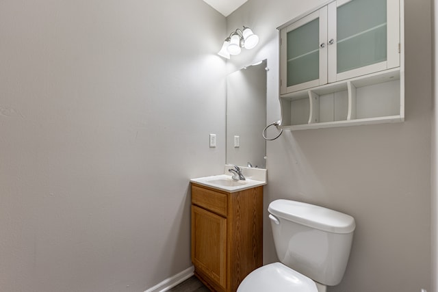 half bath featuring baseboards, vanity, and toilet