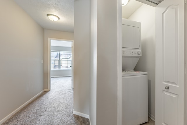 washroom with stacked washer / drying machine, laundry area, light colored carpet, and baseboards