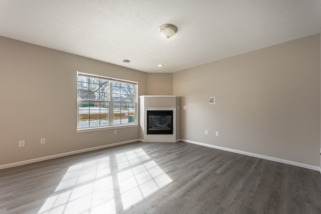 unfurnished living room featuring a glass covered fireplace, baseboards, and wood finished floors