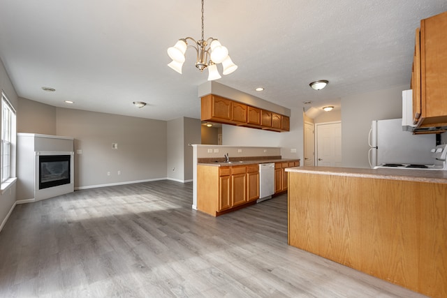 kitchen featuring white appliances, a glass covered fireplace, open floor plan, light countertops, and a sink