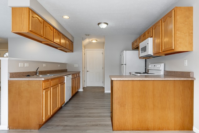 kitchen with light countertops, a sink, light wood-type flooring, white appliances, and a peninsula