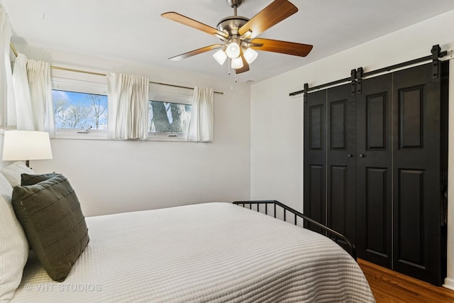 bedroom with a barn door, wood finished floors, a closet, and ceiling fan