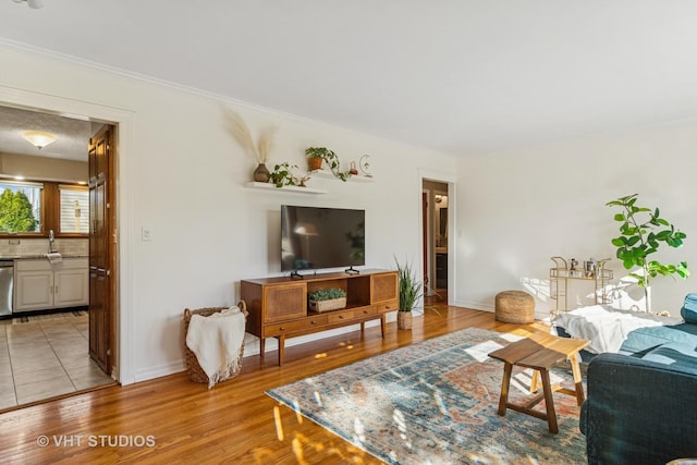 living area with baseboards, light wood-style floors, and ornamental molding