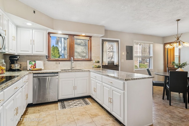 kitchen with a peninsula, a sink, stainless steel appliances, white cabinetry, and a chandelier