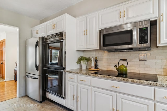 kitchen with light stone countertops, light tile patterned flooring, black appliances, white cabinets, and tasteful backsplash