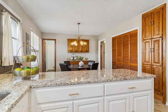 kitchen featuring a notable chandelier, pendant lighting, a textured ceiling, white cabinetry, and light stone countertops