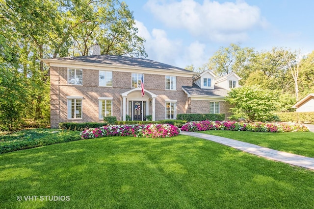 view of front of house featuring brick siding, a front lawn, and a chimney