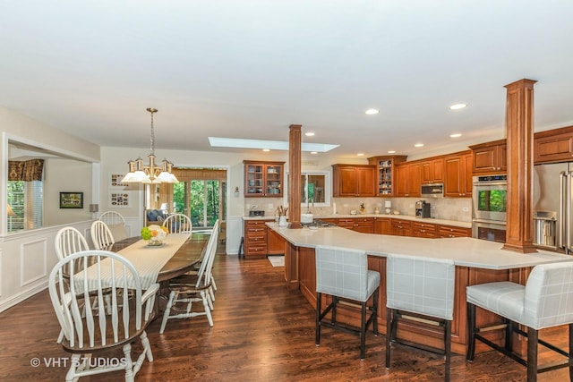 kitchen with brown cabinetry, a spacious island, appliances with stainless steel finishes, glass insert cabinets, and light countertops