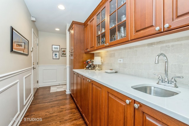 kitchen featuring light countertops, a sink, glass insert cabinets, and brown cabinets