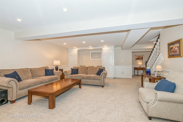 living room featuring a decorative wall, recessed lighting, light colored carpet, stairs, and wainscoting