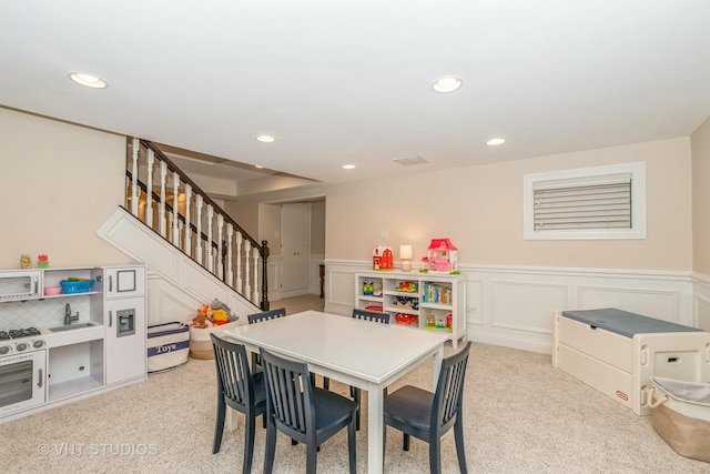 recreation room featuring light colored carpet, recessed lighting, a wainscoted wall, and a decorative wall