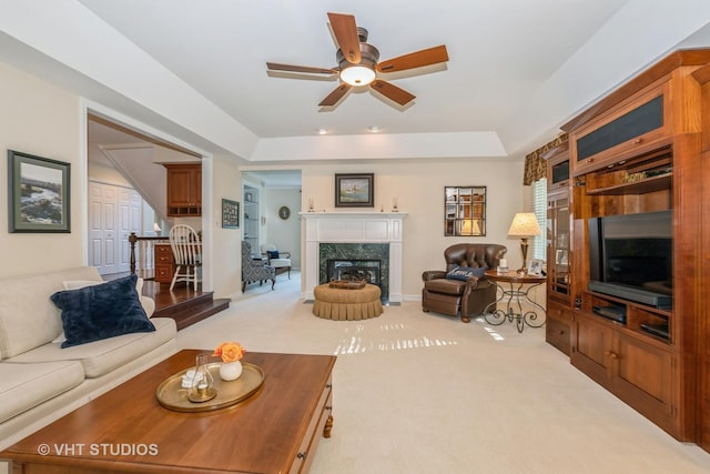 living area featuring light carpet, ceiling fan, a fireplace, and a tray ceiling