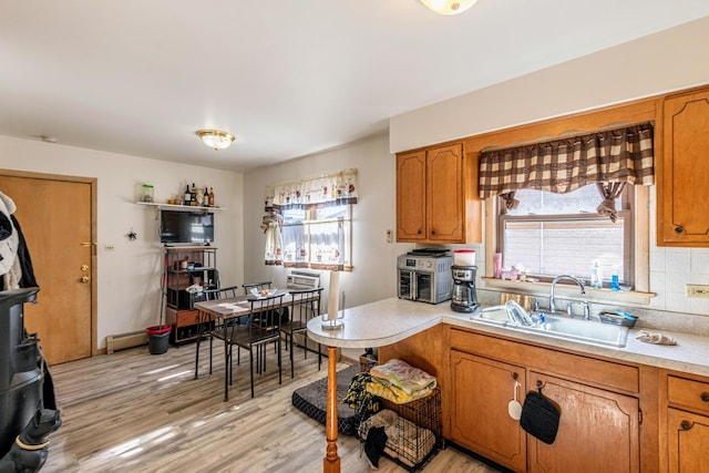 kitchen with brown cabinetry, a sink, baseboard heating, light countertops, and backsplash