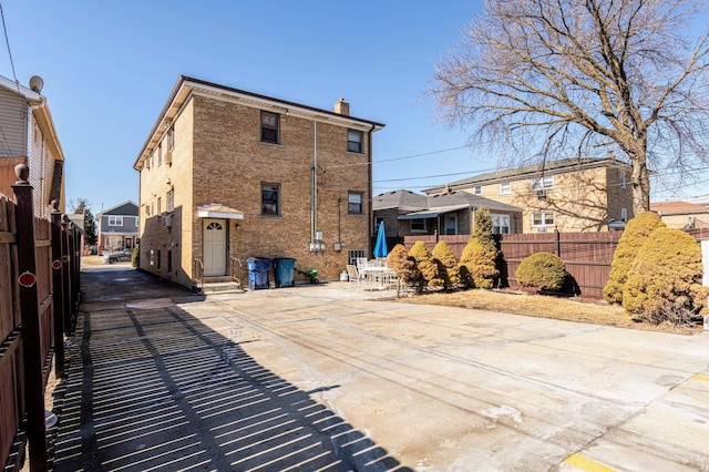 back of house featuring entry steps, brick siding, a chimney, and fence