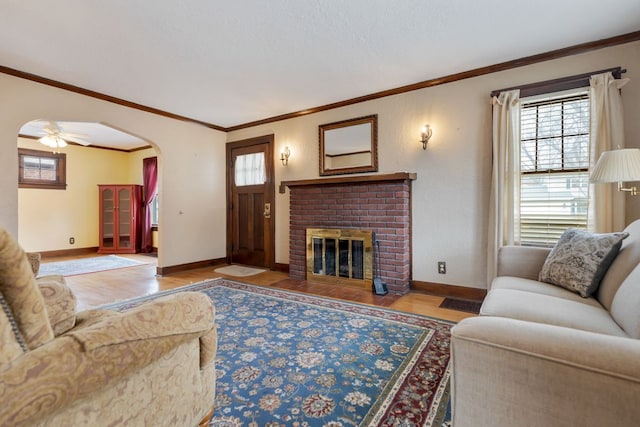 living room with light wood-type flooring, arched walkways, a brick fireplace, and baseboards