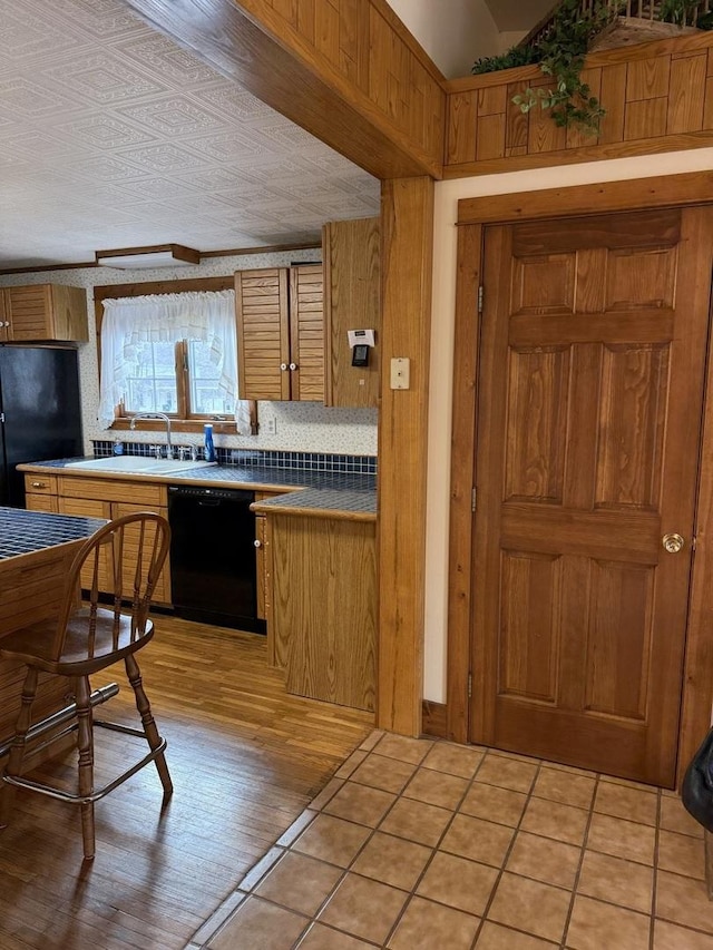 kitchen with decorative backsplash, light wood-style floors, brown cabinets, black appliances, and a sink