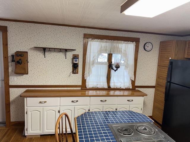 kitchen with black appliances, wallpapered walls, white cabinetry, and a wainscoted wall