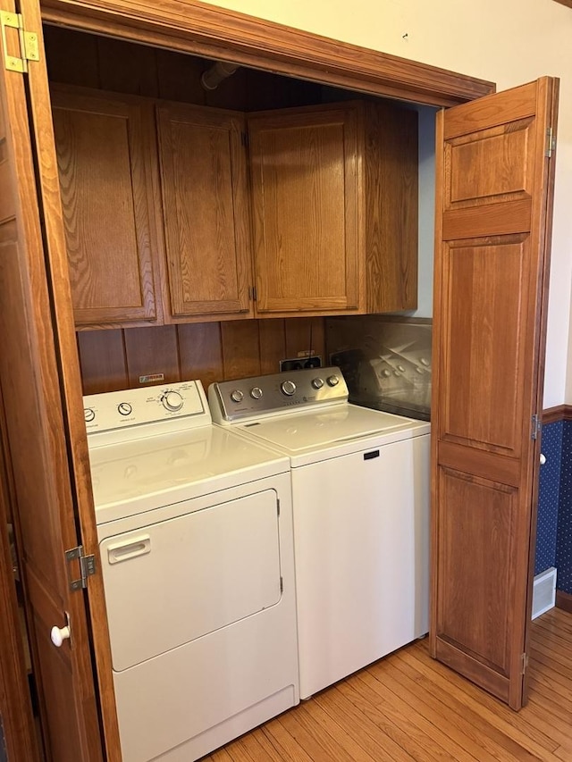 clothes washing area with cabinet space, light wood-style floors, and independent washer and dryer